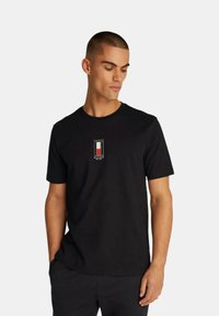 T-shirt di cotone nero a maniche corte, con un piccolo logo ricamato in rosso, bianco e blu sul petto. Texture liscia.