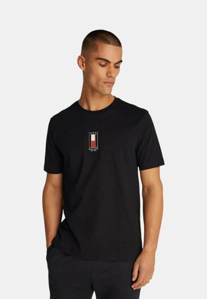 T-shirt di cotone nero a maniche corte, con un piccolo logo ricamato in rosso, bianco e blu sul petto. Texture liscia.