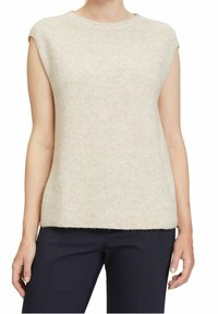 Top in maglia beige senza maniche indossato con pantaloni blu scuro, mostrato dalla scollatura ai fianchi su una persona in piedi.