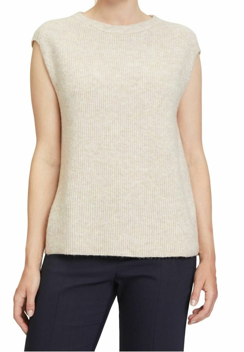 Top in maglia beige senza maniche indossato con pantaloni blu scuro, mostrato dalla scollatura ai fianchi su una persona in piedi.