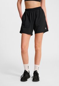 Svarta träningsshorts med ett elastiskt midjeband, två sidofickor och en liten logotyp vid fållen. Bärs med svarta skor och vita strumpor.