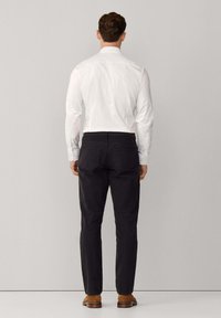 Wit overhemd met lange mouwen en een spitse kraag, gecombineerd met zwarte broek en bruine schoenen. De stof oogt glad en heeft een getailleerde pasvorm.