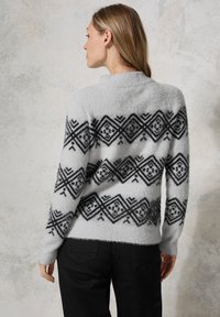 Lichtgrijze trui met een zwart geometrisch patroon, met een comfortabele textuur en een ronde halslijn. Gecombineerd met zwarte broeken.