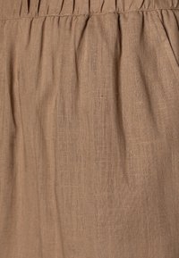 Tissu en lin brun avec une texture douce et de légères rides, présentant des détails froncés en haut. Matière légère et respirante.