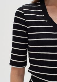 Svart ribbat linne med vita horisontella ränder, korta ärmar och V-ringning, med fokus på textur och mönster.