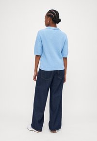 Pull azul claro tricotado com gola, mangas curtas e acabamento texturizado, combinado com jeans escuros folgados.