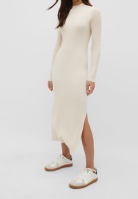 Robe midi en tricot côtelé, beige crémeux, avec des manches longues et une fente sur le côté. Associée à des baskets blanches avec des accents et des lacets beiges.