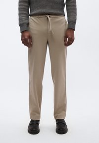 Pantaloni beige a sigaretta in tessuto morbido, con coulisse elastica in vita, texture liscia e tasche laterali.
