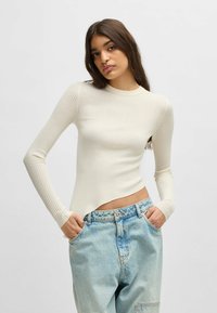 Top a maniche lunghe a coste in bianco sporco, con un design attillato e orlo curvo. Abbinato a jeans a vita alta di colore blu chiaro.