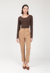 Braunes Langarmoberteil kombiniert mit beigen maßgeschneiderten Hosen mit Seitentaschen und umgeschlagenem Saum, ergänzt durch braune spitze Schuhe.