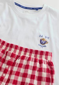 Hvid T-shirt med broderet kop og teksten "But first, coffee" kombineret med røde og hvide ternede pyjamasshorts med hvide knapper.