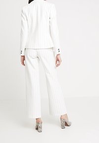 Bílý pruhovaný oblek s přiléhavým sakem a širokými kalhotami. Boty mají texturovaný vzor připomínající hadí kůži a vysoký silný podpatek.