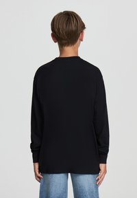 Maglietta nera a maniche lunghe con scollatura tonda, tessuto morbido e vestibilità rilassata, abbinata a jeans a gamba larga blu chiaro.