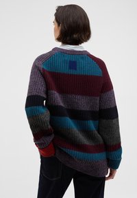 Knit sweater in multi-colored stripes: maroon, teal, gray, and navy with textured fabric and ribbed cuffs. Back features a square accent.