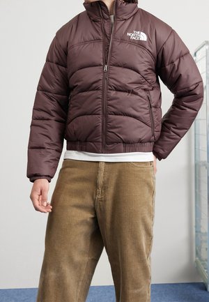 Bordeaux pufferjack met een hoge kraag, ritssluiting en subtiele stikseldetails. Voorzien van zijzakken en een logo op de linkerborst.