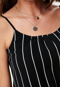 Débardeur noir à rayures verticales blanches, en tissu texturé. Il présente de fines bretelles et un col plissé. Colliers argentés superposés.