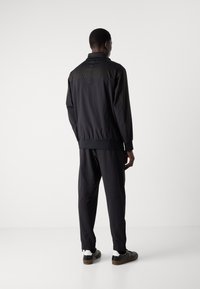 Black athletic jacket with a high collar, zip closure, and matching trousers. Both have a smooth, lightweight texture and fitted cuffs.
