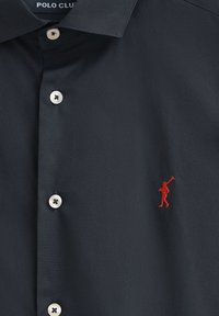 Polo shirt navy con colletto button-down, placca dei bottoni argento e una piccola figura rossa ricamata che tiene una mazza da golf sul petto.