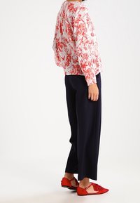 Blusa floreale in rosso e bianco, abbinata a pantaloni larghi blu navy e ballerine rosse con dettagli frangi.