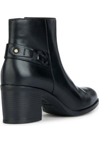 Bottine en cuir noir avec bout rond, talon texturé, sangle en cuir tressé et un petit bouton décoratif sur le côté.