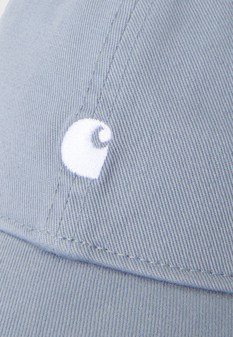 Nahaufnahme von hellblauem Stoff mit weiß gesticktem Carhartt-Logo auf der Vorderseite einer Kappe.