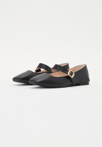 Ballerines noires à bout pointu, avec une sangle entrecroisée et une boucle accentuée en or, fabriquées en cuir lisse. Semelle plate.