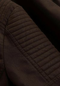 Hnědá kožená bunda s prošívanými detaily na ramenou, texturovaným povrchem a výrazným prošíváním, zdůrazňující odolnost a design.