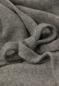 Tejido de punto gris con un detalle de lazada atada, superficie texturizada y acabado suave y aterciopelado. El tejido se presenta ligero y acogedor.
