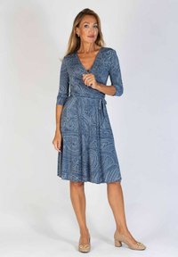 Niebieska sukienka w paisley z rękawami o długości trzech ćwiartek, do kolan, z paskiem do przewiązania. Noszona z jasnobeżowymi butami na słupku.