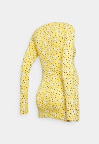 Top de mangas longas amarelo com bolinhas pretas e estampa floral, apresentando um design justo e uma textura suave.