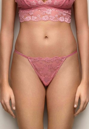 Mujer vistiendo un conjunto de lencería de encaje rosa a juego, que incluye un bralette y un tanga, mostrado desde la parte superior de los muslos hasta debajo del pecho.