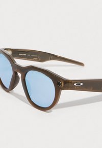 Ruske plastikkesüt med oktagonale rammer, blå linser og metalliske logo-aksenter. Har unike teksturerte detaljer på armene.