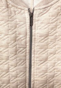 Krémová prošívaná bunda na zip se strukturovaným vzorem, stříbrným zipem a žebrovaným límcem, s hladkým povrchem látky.