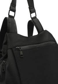 Mochila negra de nailon que cuenta con correas ajustables, un bolsillo delantero con cremallera y una textura suave con un diseño elegante y hardware minimalista.