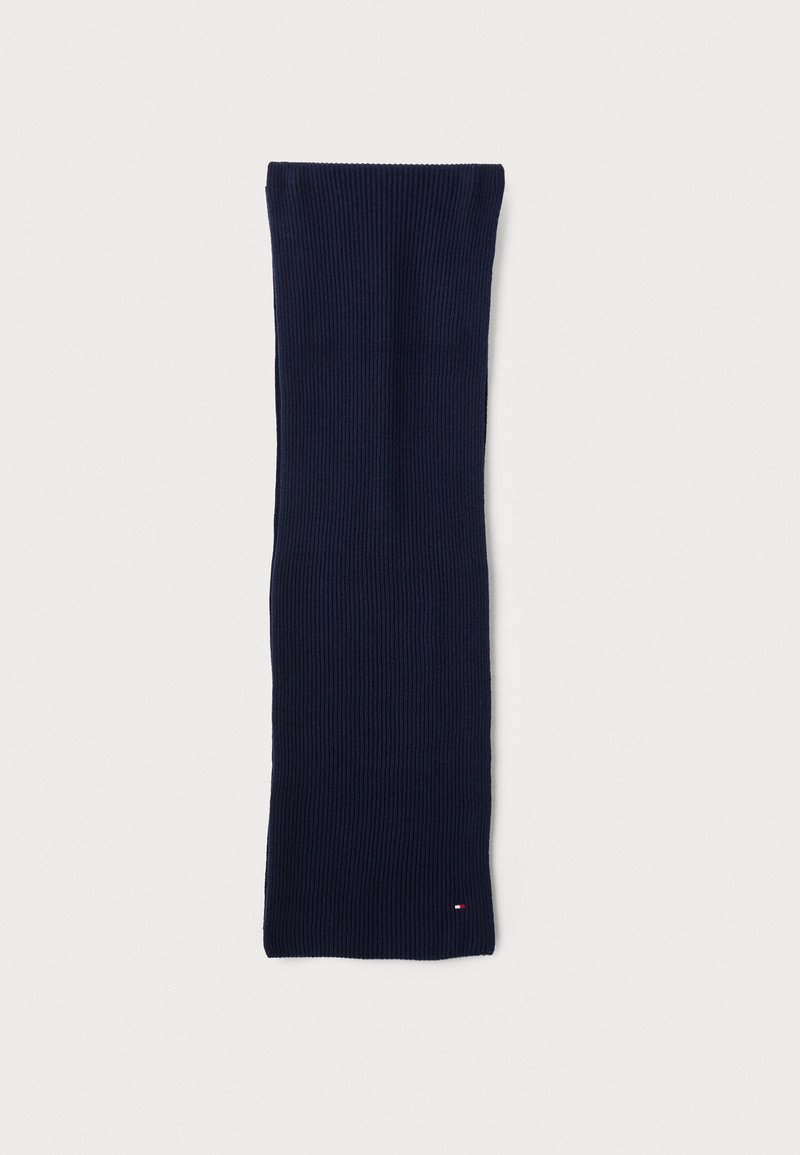 Knitted navy scarf with a ribbed texture, elongated shape, and small logo detail in red, white, and blue at the bottom corner.