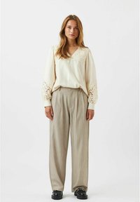 Blusa crema con dettagli in pizzo lungo il collo e le maniche, abbinata a pantaloni beige a righe e scarpe nere chunky.