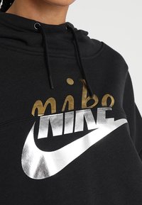 Svart hoodie med guld- och silverfärgad Nike-logga och swoosh, med dragsnören vid halsen.