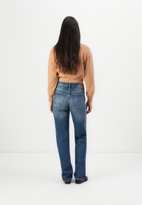 Blå raka jeans med medelhög midja, bakfickor med böjd sömnad, bärs med en beige sweatshirt. Slät denimtextur.