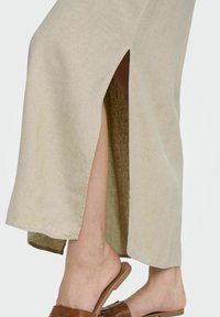 Falda de lino beige con aberturas laterales, con una textura suave y un caída fluida. Combinada con sandalias planas de tejido marrón.