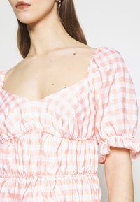 Abito in vichy rosa e bianco con scollatura quadrata, maniche a sbuffo, vita elastica e dettagli arricciati sul corpo e sulle maniche.