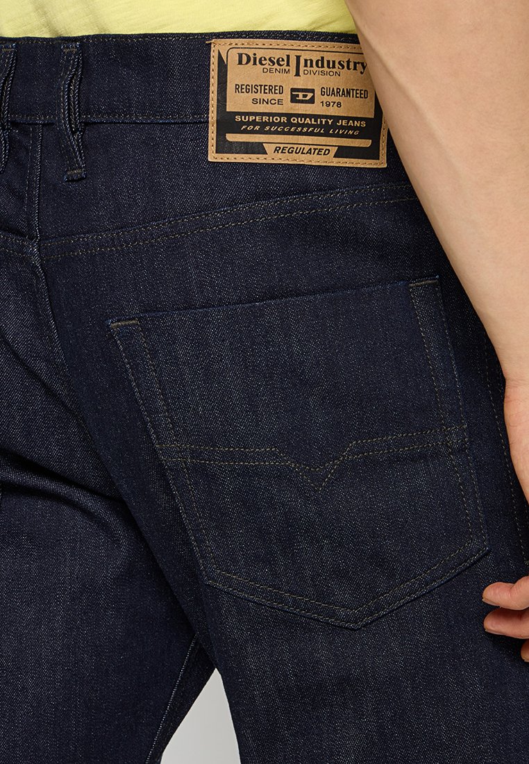 Jeans in denim blu scuro con superficie testurizzata, dotati di etichetta in pelle e tasche posteriori con un distintivo design di cucitura a forma di V.