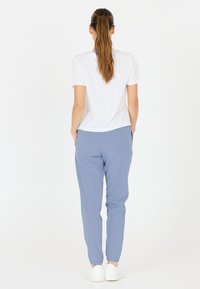 Witte top met korte mouwen gecombineerd met lichtblauwe tapered broeken; de broeken hebben zijzakken en elastische enkels; gladde textuur.