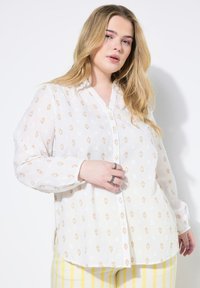 Camicia bianca con bottoni, realizzata in un tessuto texture, con un delicato motivo floreale nei toni dell'arancio e del giallo tenue. Presenta maniche lunghe e colletto.