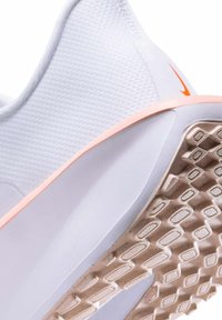 Witte sportieve schoen met een gestructureerde mesh bovenkant, een oranje accent op de hiel en een rubberen zool met een geprofileerd loopvlak.
