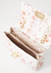 Handväska med blommönster som har en strukturerad form, en texturerad vit yta, guldhardwaredetaljer och en öppen insida med en dragkedjeficka.