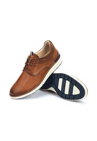 Zapatos de cuero marrón con un acabado liso, detalles perforados, diseño de cordones y una entresuela blanca contrastante con una suela de goma negra.