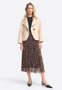 Beige krajkový kabát z vlny s velkými klopami, kombinovaný s plisovanou maxi sukní s leopardím potiskem a černými lakovanými vysokými botami.