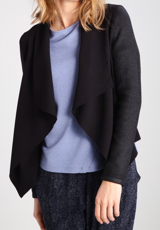Czarny kardigan z narzutką na jasnoniebieską bluzkę, z teksturowanymi czarnymi rękawami. Ubranie charakteryzuje się luźnym, płynącym krojem i otwartym przodem.