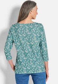 Turquoise gestreepte top met een geometrisch ontwerp, voorzien van driekwartmouwen en een brede halslijn, gemaakt van een zachte stof.