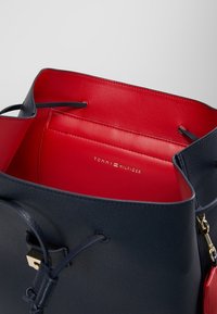 Borsa a secchiello in pelle blu navy con interno rosso. Presenta corde regolabili e accessori in tono oro con logo impresso sull'interno.